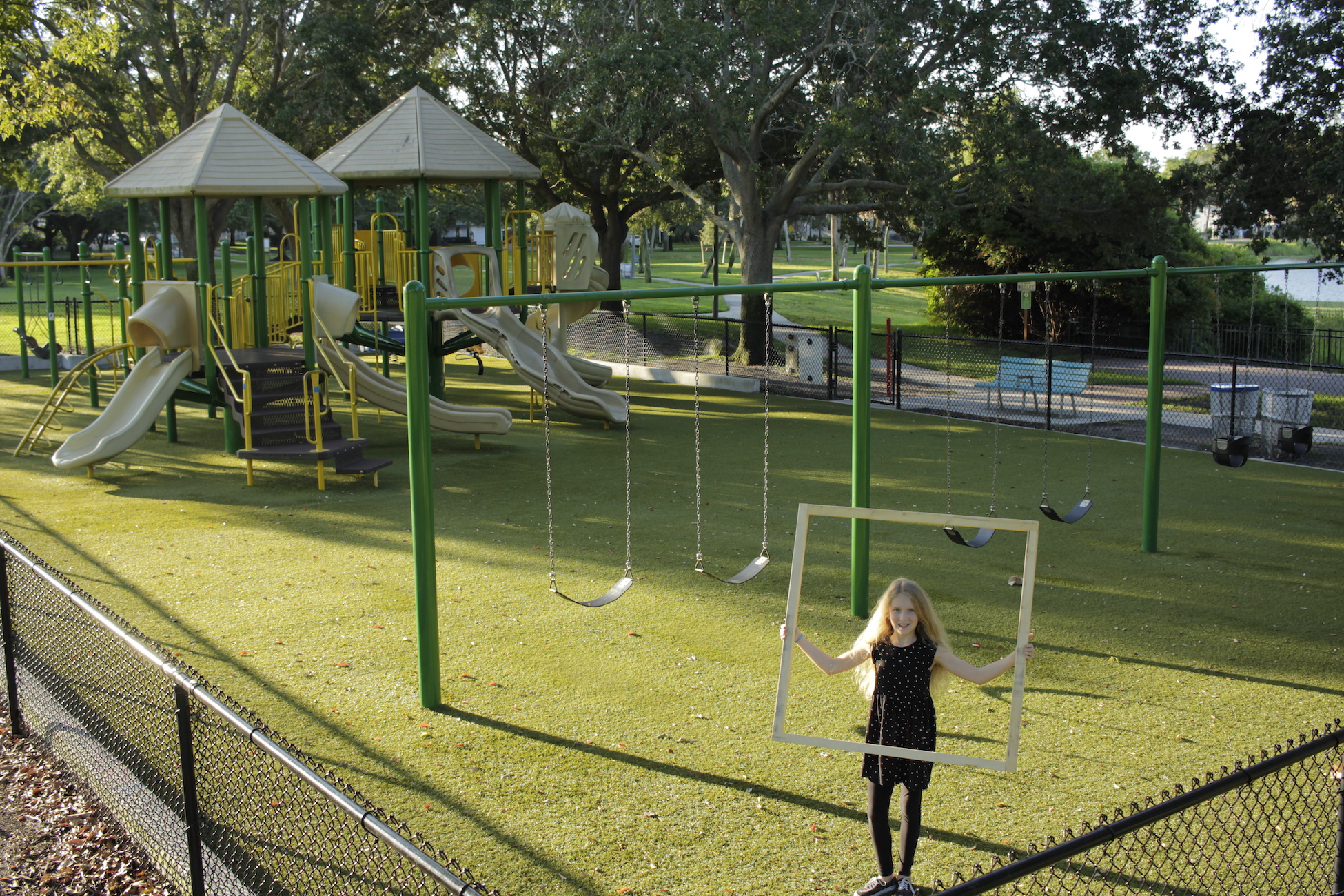 Photograph. Person holding large square. Playground in background.