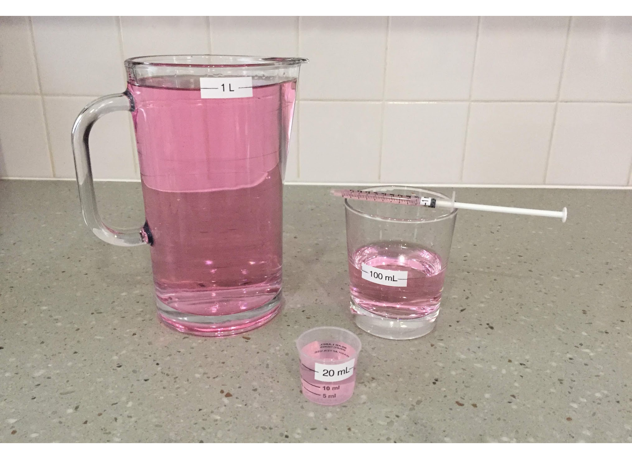 picture of pink liquid in 4 different size containers. Volumes of liquid, 1 liter, 100 milliliters, 20 milliliters, and some in a medicine dropper.