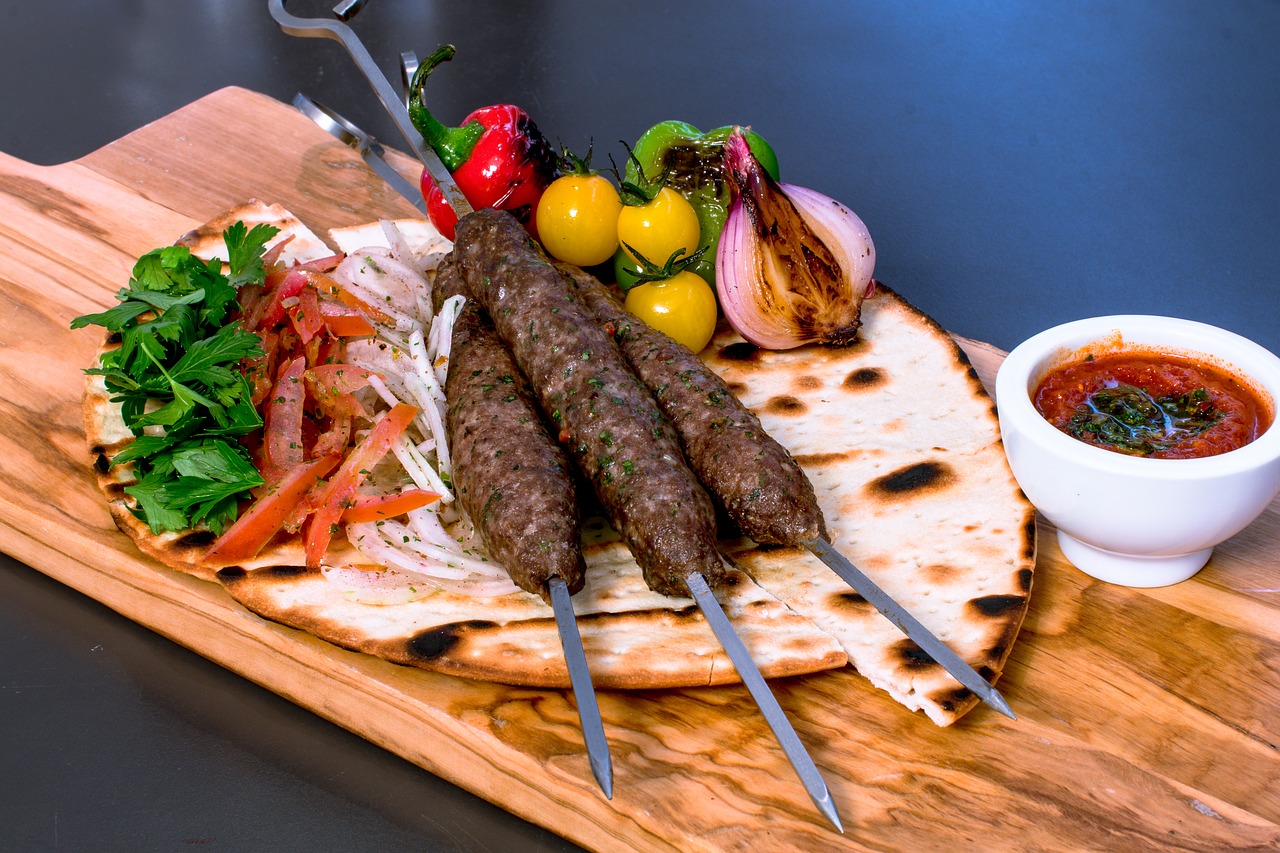 Skewers of meat and piles of vegetables on top of pita bread, sauce on side 